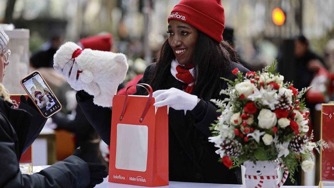 Smiling woman in winter holiday wear, packing up holiday bags as part of Teleflora's Wish Bear Workshop Benefitting Make-A-Wish at Rockefeller Center.