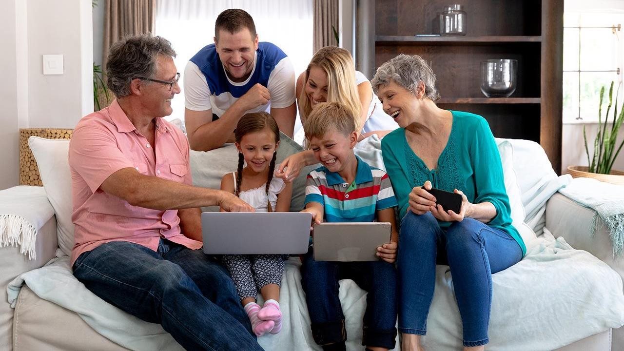 Three generations of a family sitting on the couch with a laptop, tablet and phone.