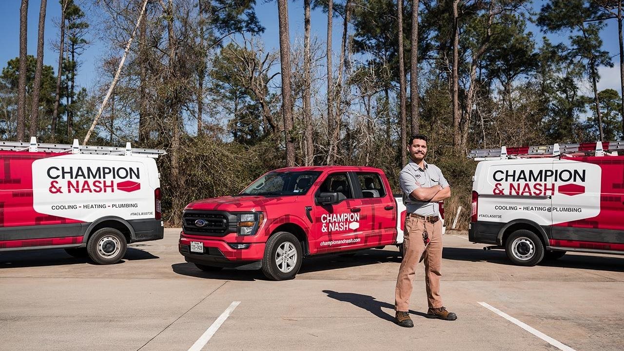 Representative from Champion & Nash standing in a parking lot with a couple of company vans and a truck.