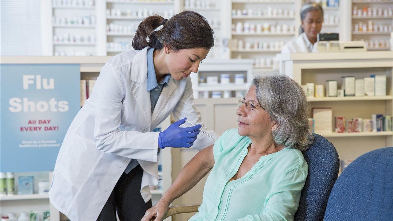 Mujer mayor que recibe la vacuna contra la gripe de una farmacéutica. Los pacientes pueden acudir sin cita previa a su Walgreens local o programar una cita en línea a través de Walgreens.com/ScheduleVaccine.