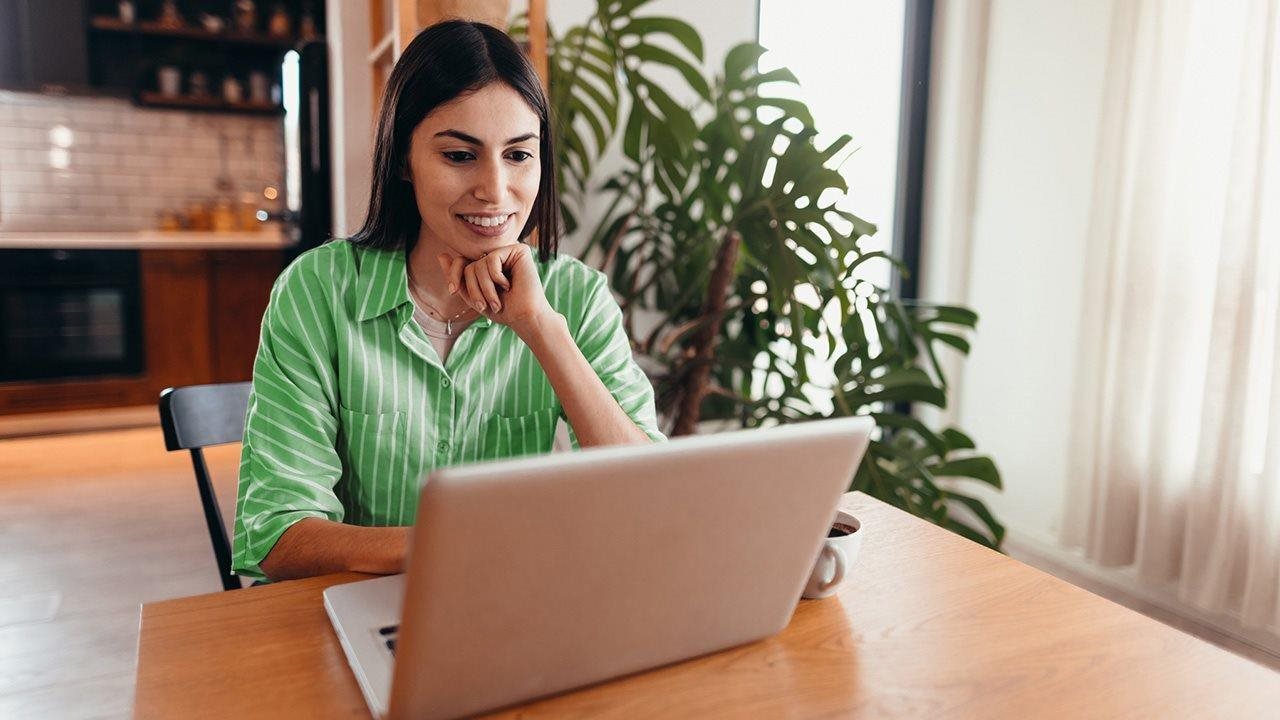 A woman rests her chin on her hand as she uses her laptop.
