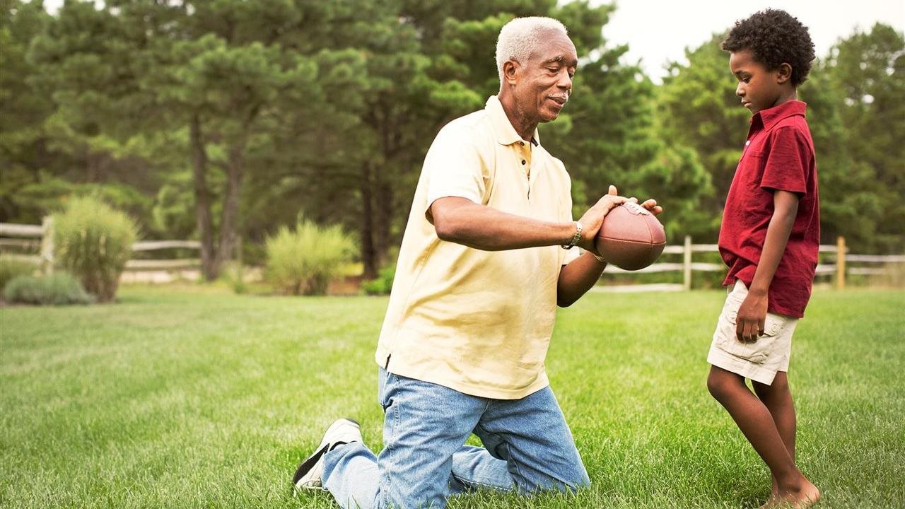 Grandfather teaching grandson how to hold a football in the backyard on a summer day.