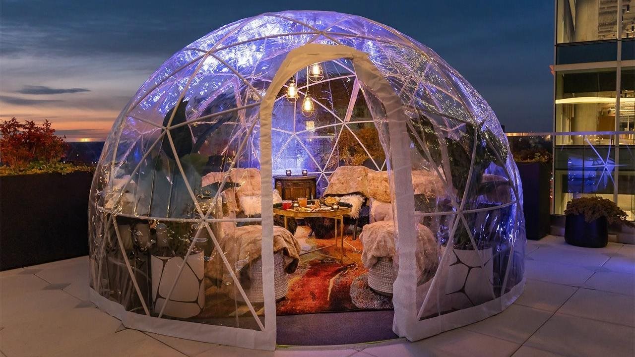 Hip flask rooftop igloo furnished with rugs, chairs, and footstools in the evening.