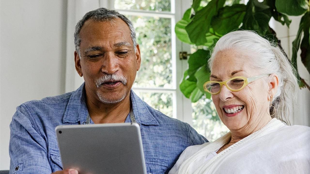 Pareja mirando una tableta mientras sentados en el sofá. Un plan D-SNP, Plan de Necesidades Especiales Duales, es un plan Medicare Advantage para personas que tienen Medicare y Medicaid.