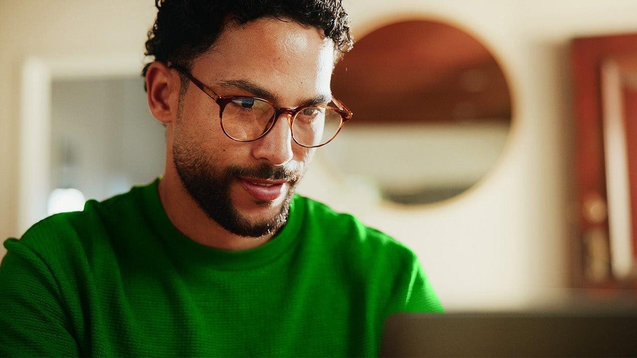 Man in glasses and a green sweater looking at laptop. To learn more about 100% fiber internet, visit ZiplyFiber.com
