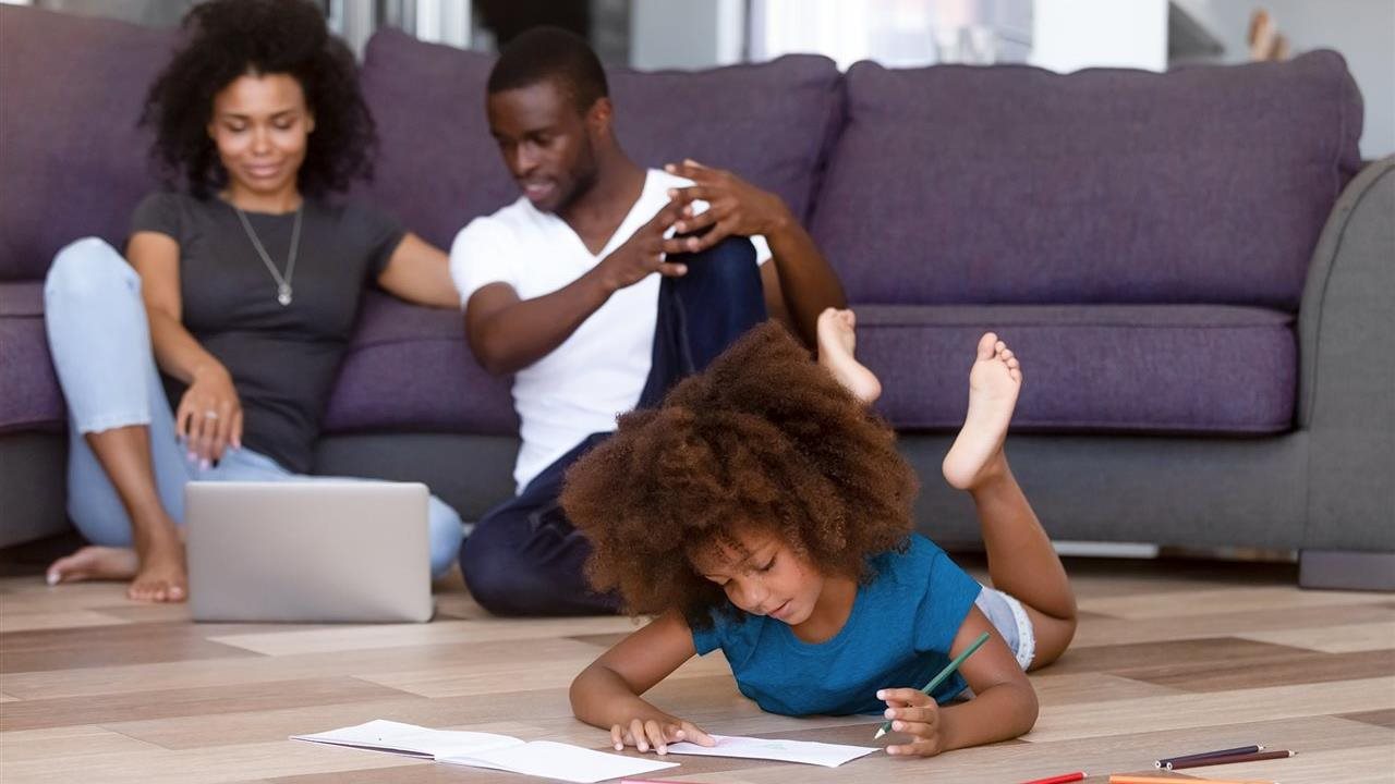 Mom, dad and young daughter sit on the floor in their livingroom. Professionals Alliance can help you find a radiant heat installer.
