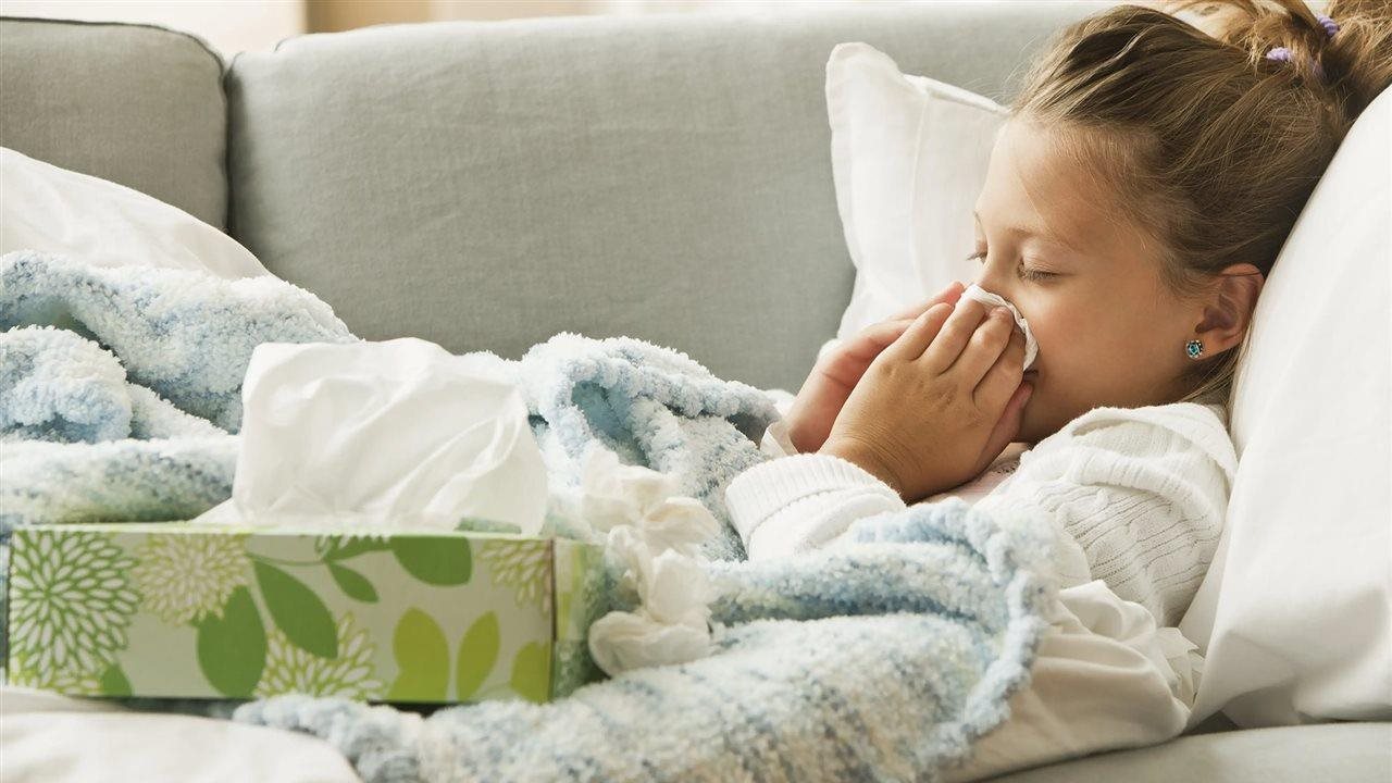 Girl blowing her nose while laying on the couch who might benefit from a fan like the Whisper Symphony Exhaust Fan, an energy-efficient solution that improves airflow, so you won't have to worry about humidity and mold impacting your IAQ.
