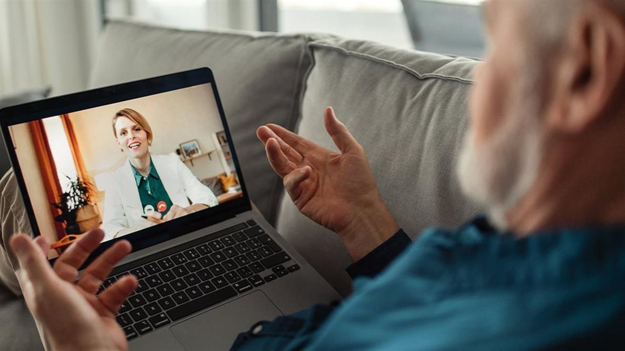 Senior man using his laptop for a vitual appointment with a doctor from his couch at home.