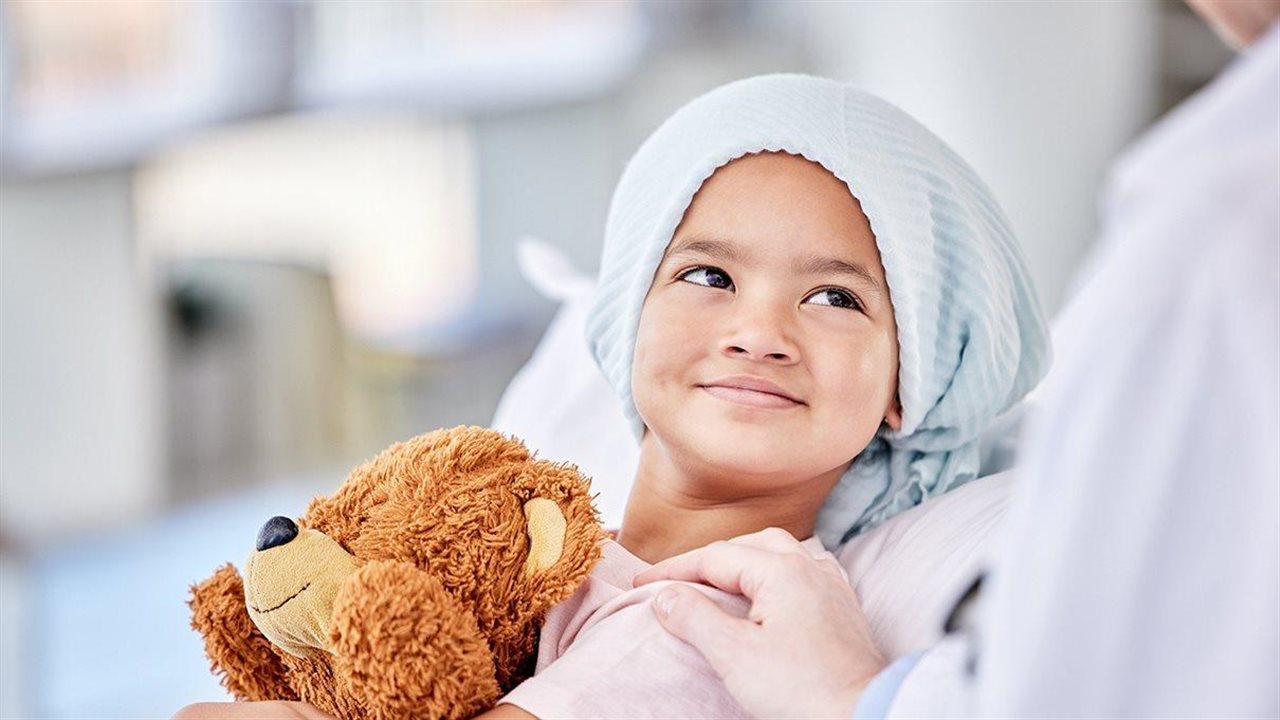 A little girl in the hospital smiles as a doctor rests their hand on her shoulder.