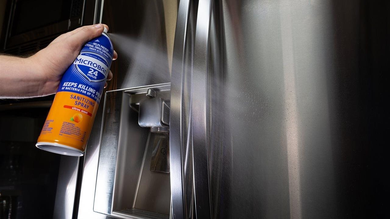 Person spraying a refrigerator with Microban 24 sanitizing spray.