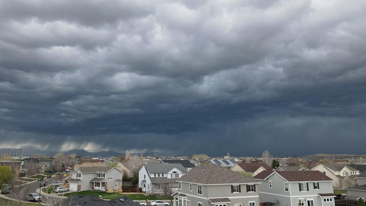 Overcast skies over a neighborhood of two-story houses with rainfall in the distance.