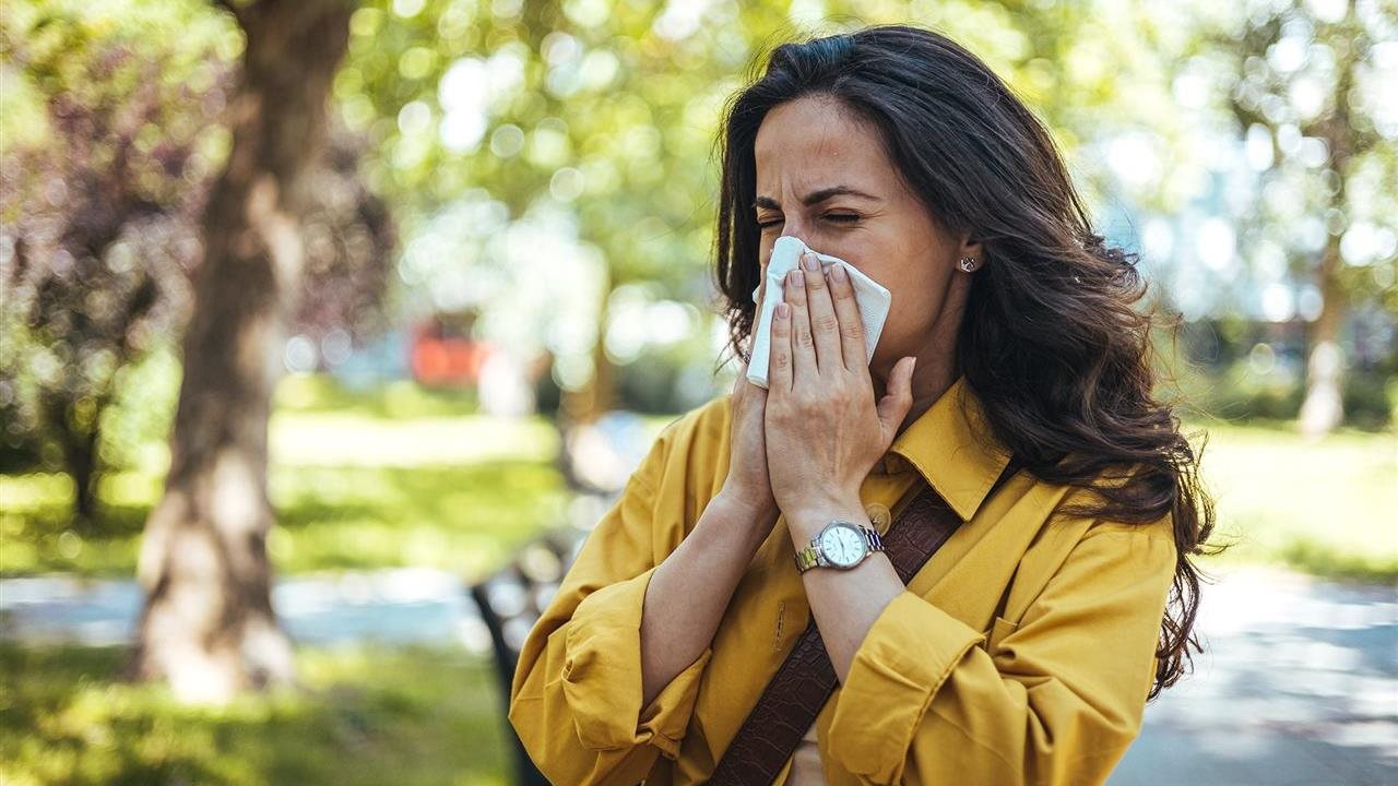 Woman blowing her nose while in a park. Dr. Pescatore recommends Pycnogenol® to his patients.