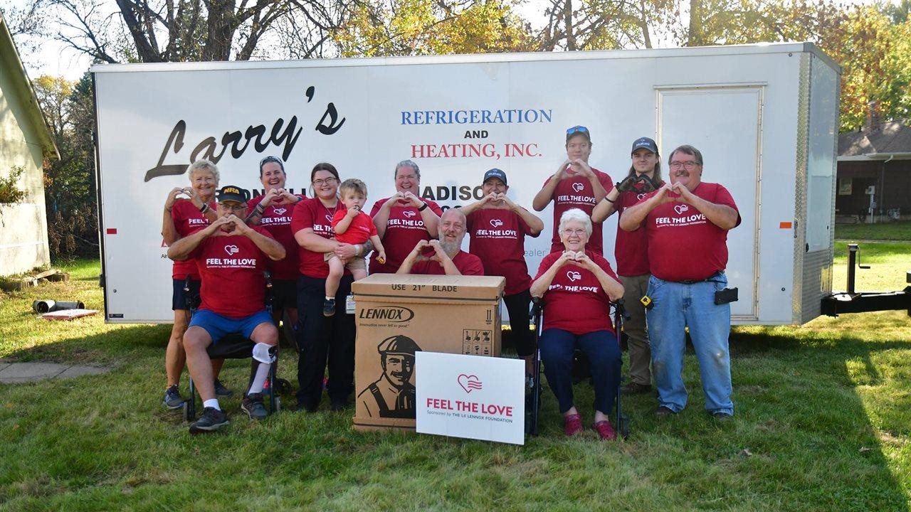 People in red shirts that say "Feel the love" standing in front of Larry's Refridgeration and Heating trailor next to Lennox product.