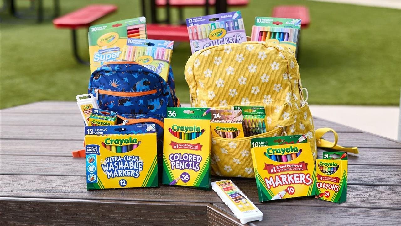 A park bench with backpacks filled with Crayola supplies: crayons, colored pencils, markers, paint and Crayola clicks.