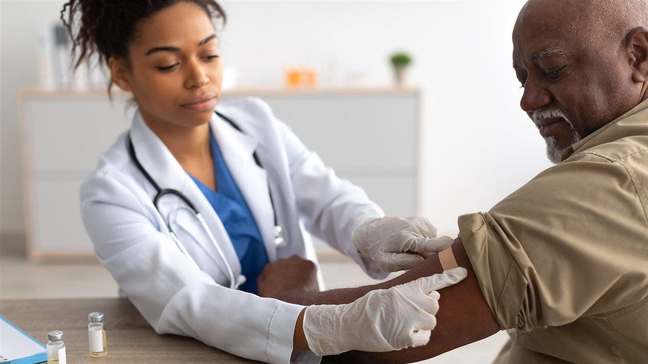 Hombre mayor recibiendo la vacuna contra la gripe de una proveedora de atención médica en una clínica.