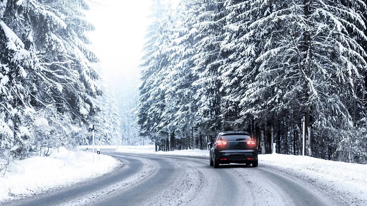 Person in a car, with new Hankook tires, driving on a curvy, snow-covered road near a forest with snow-covered pines.
