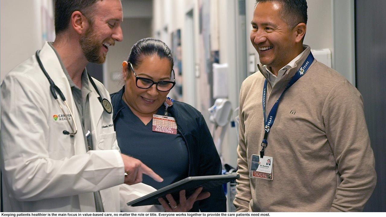 Health care professionals discussing information on tablet in a hallway of a clinic.