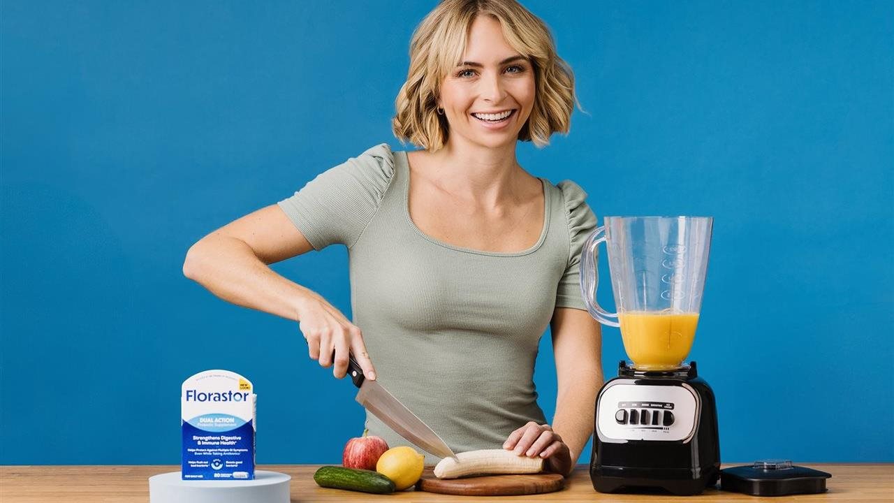 Woman cutting up fruits and vegetable next to a blender and a container of the daily probiotic  Florastor Dual Action Probiotic*. This wellness product supports digestive and immune health and doesn't require refrigeration.
