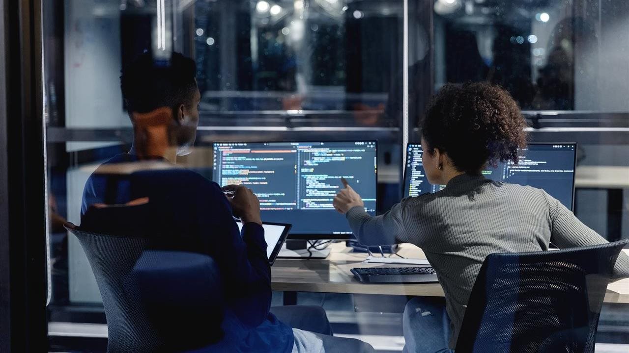 Two people working on a computer program. DeVry students can participate in the Future Cyber Defenders Scholars Program,