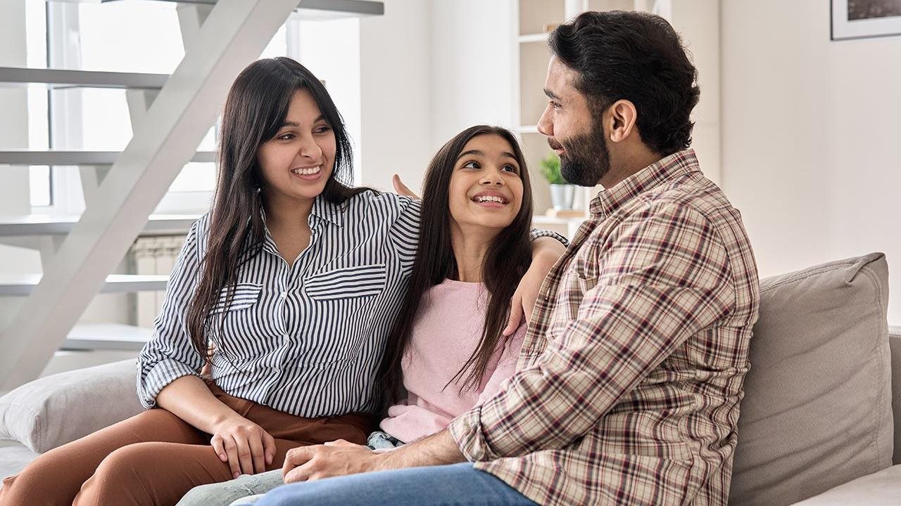 Mom and Dad sitting on the couch with their daughter talking about college plans.