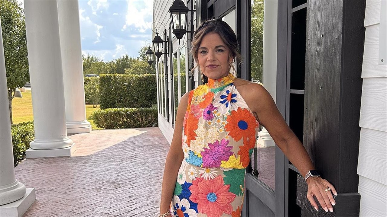 Adrianne in a floral dress standing on the porch of a beautiful venue.