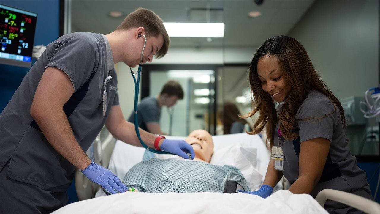 Two students transporting a patient replica on a gurney through a hospital.