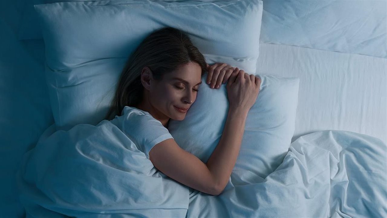 Woman sleeping peacefully on white sheets in bed. Natrol contains melatonin which may help support your natural sleep cycle.