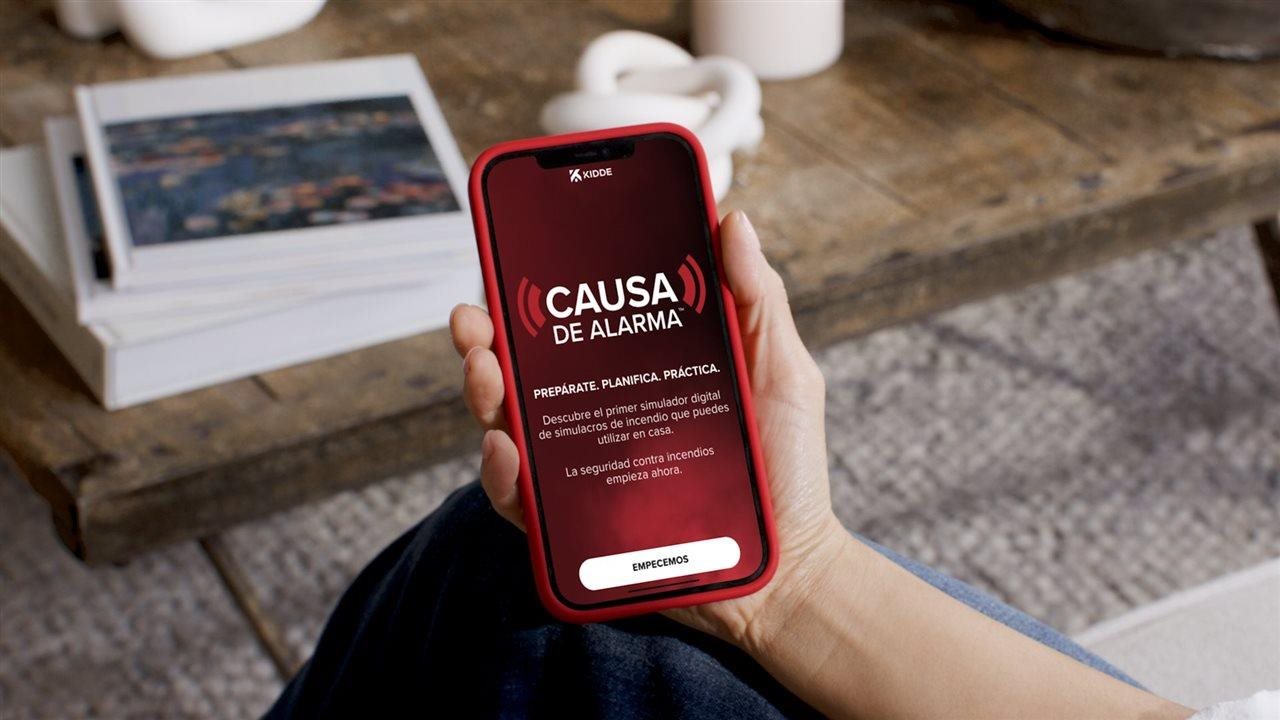 Persona sosteniendo un celular con una aplicación que permite al usuario practicar simulacros de incendio en casa.