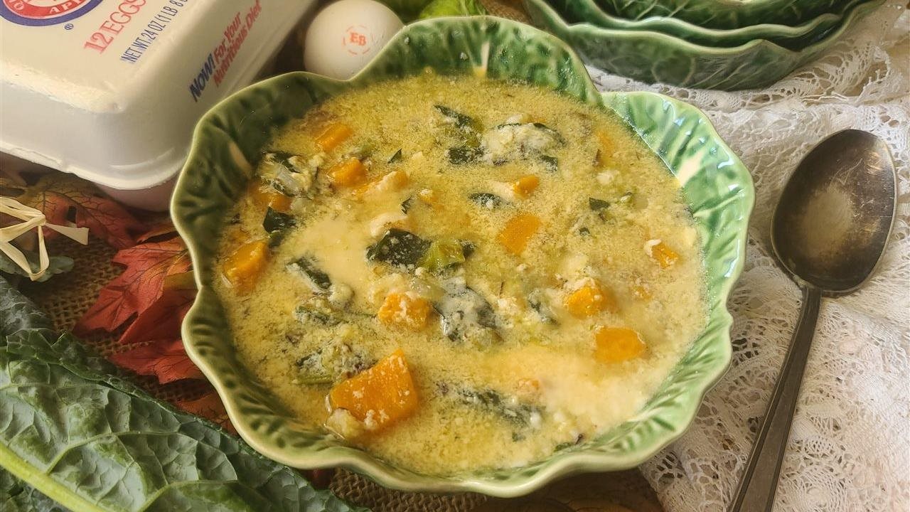 Sopa Stracciatella de cosecha servida en un tazón de estilo antiguo y un cartón de huevos Eggland's Best en una mesa decorada con adornos otoñales.