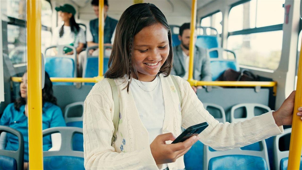 Una adolescente usa un móvil en un autobús escolar. Metro by T-Mobile ayuda a las familias a mantenerse conectadas.
