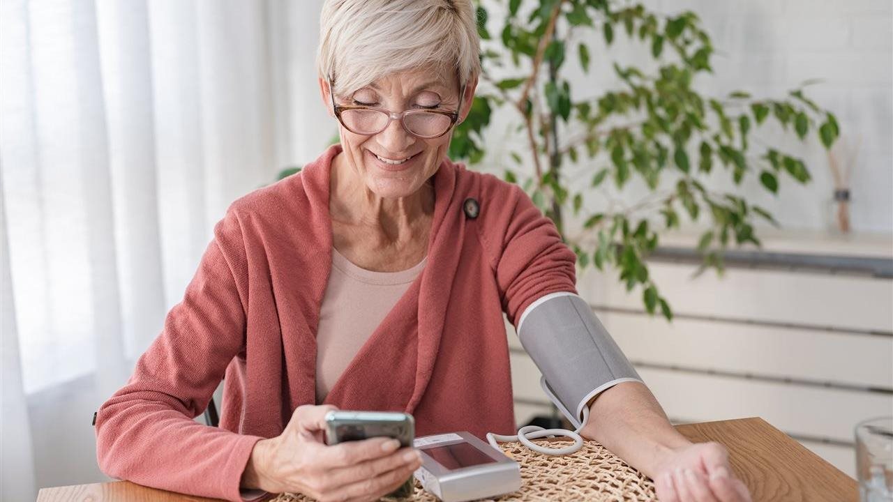 Senior woman takes blood pressure and uses phone app. Anthem Whole Health connects individual’s healthcare touchpoints.