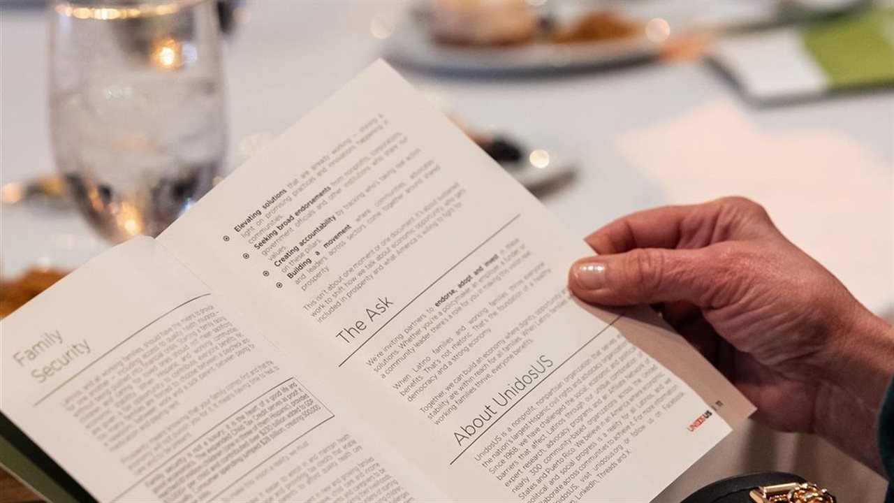 Woman reading a pamphlet, that talks about Unidos, while dining in a beautiful restaurant.