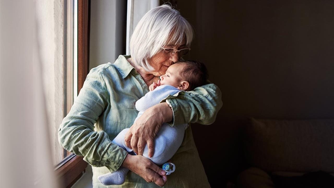 Grandmother holding a baby and kissing his forehead. An AARP membership can help seniors save money.