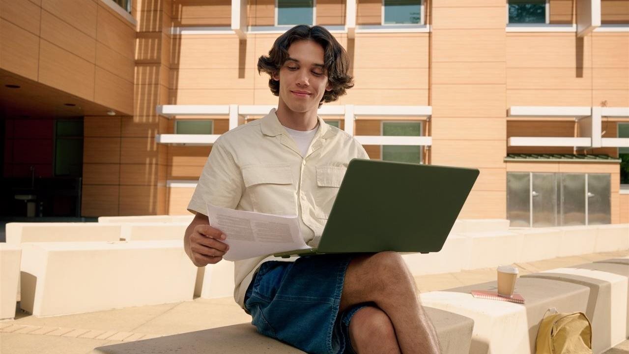 Man on a bench, holding a tax form while using laptop. Credit Karma and TurboTax help consumers make financial decisions.