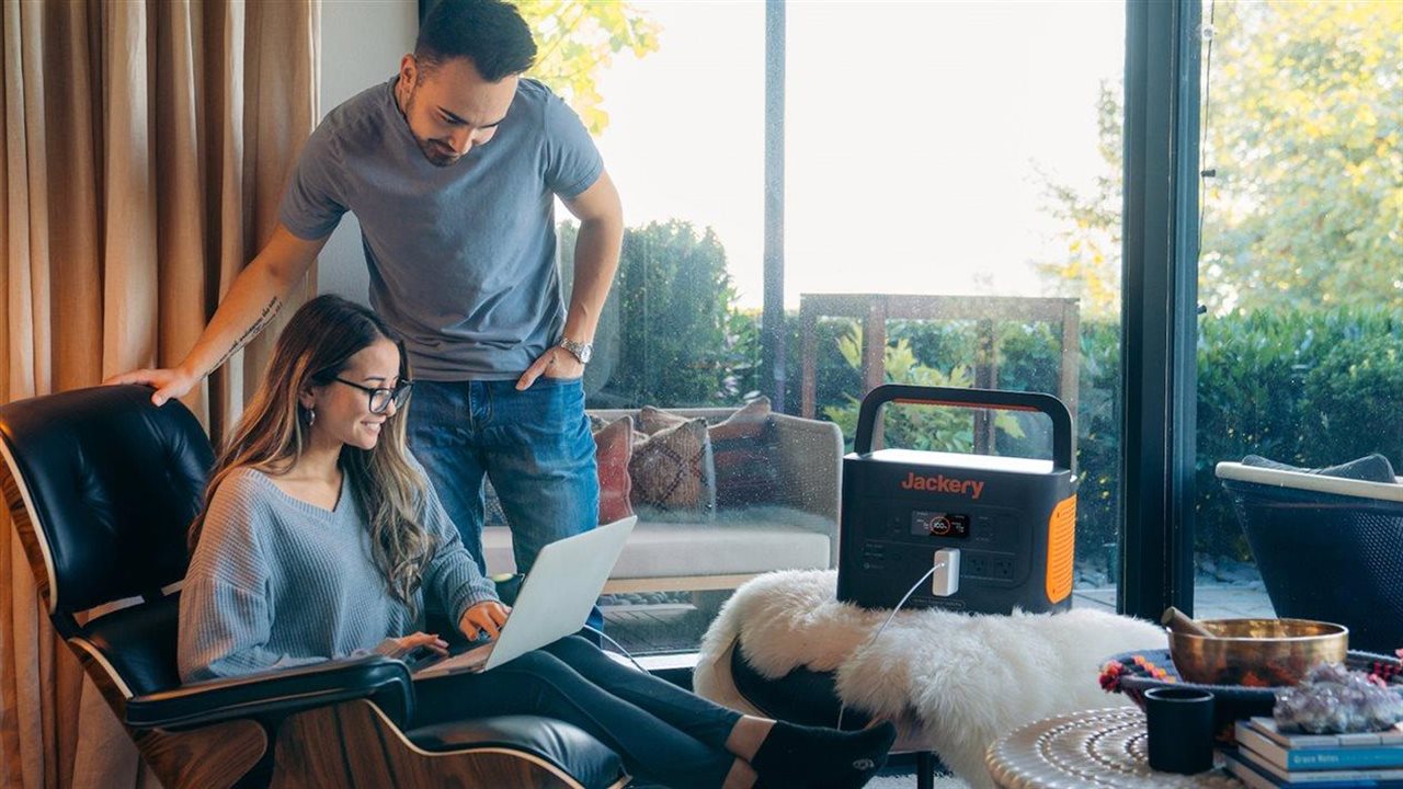 Couple using a laptop at home while it is plugged in to a Jackery power back-up device.