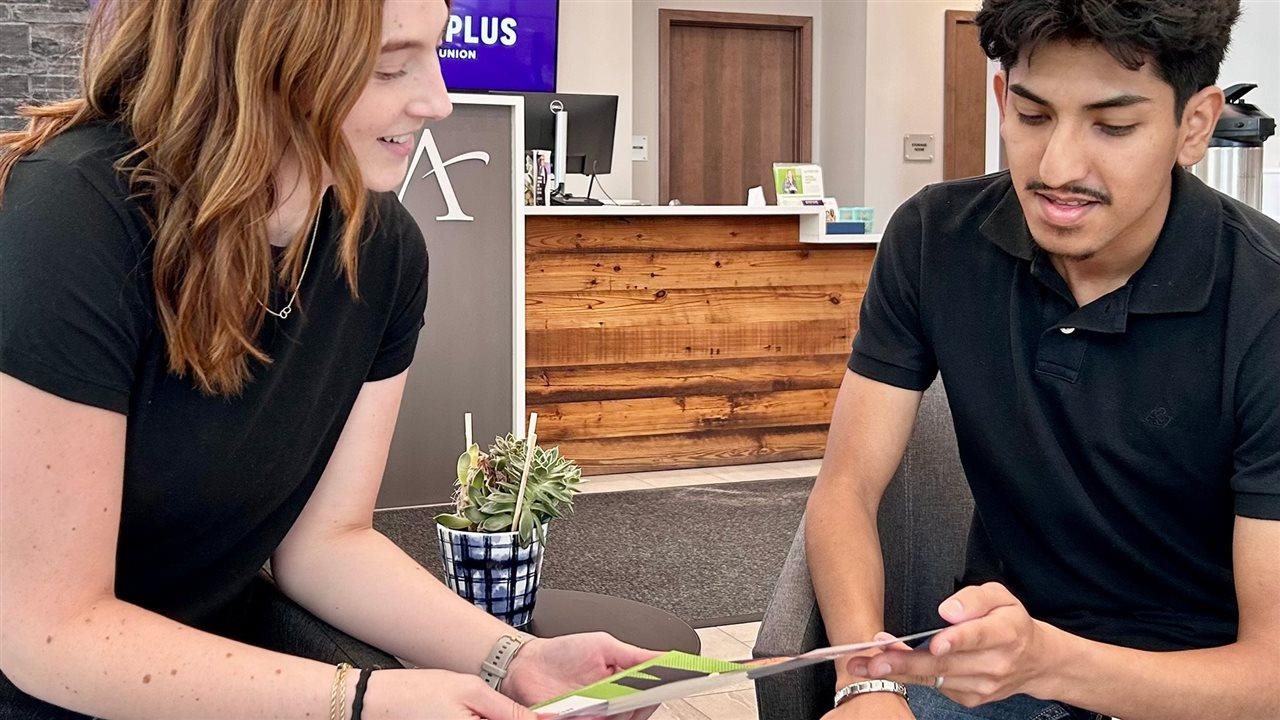 Woman showing a young man a brochure. Affinity Plus Federal Credit Union is a member-owned cooperative.