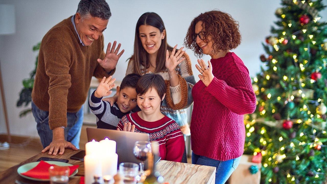 A family gathered around a laptop waves to the person they're talking to on it, with a Christmas tree behind them.