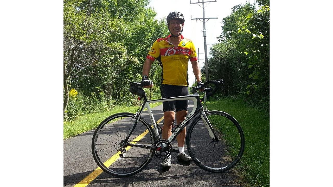 Daryl Kunz smiles and poses behind his bicycle.