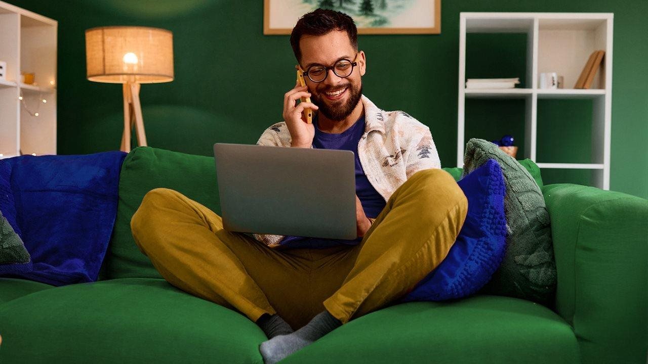 Man using Ziply Fiber internet for both his laptop and his phone from the couch in his living room.