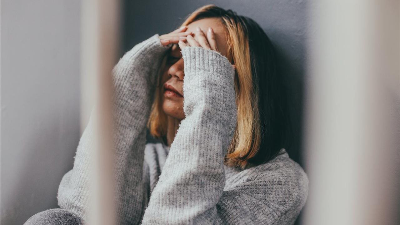 Woman in sweater covering her face with her hands