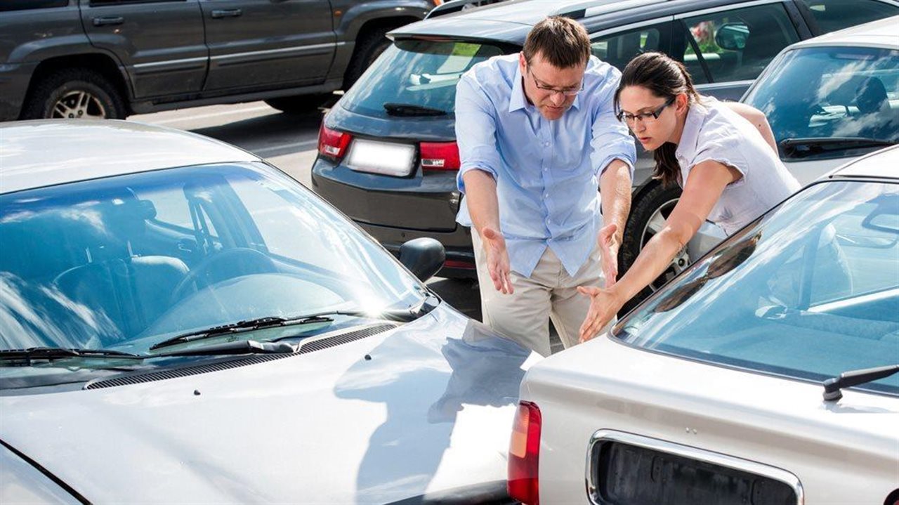 Man and a woman outside examining the damage to their cars after an accident.
