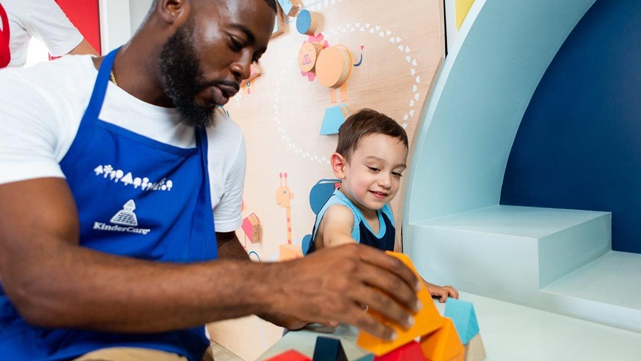 Male KinderCare teacher working with small child and plastic blocks.