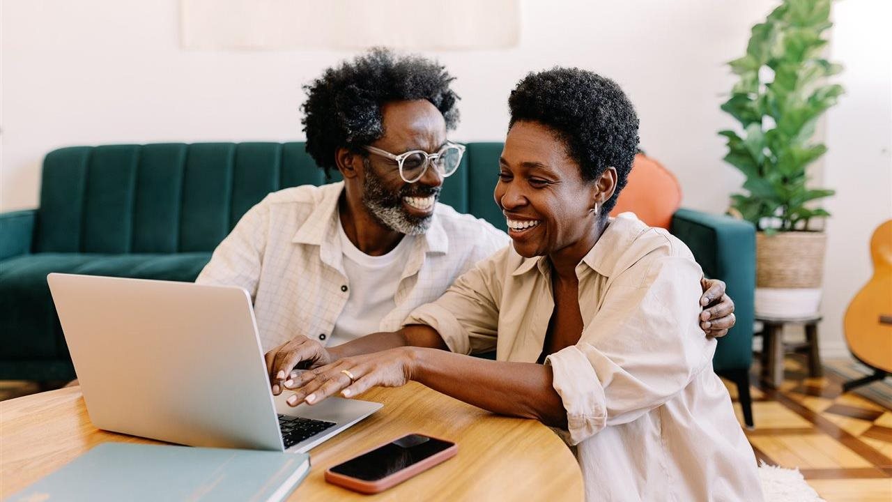Smiling couple on their laptop in the livingroom. AARP members can save on an American Home Shield® home warranty.
