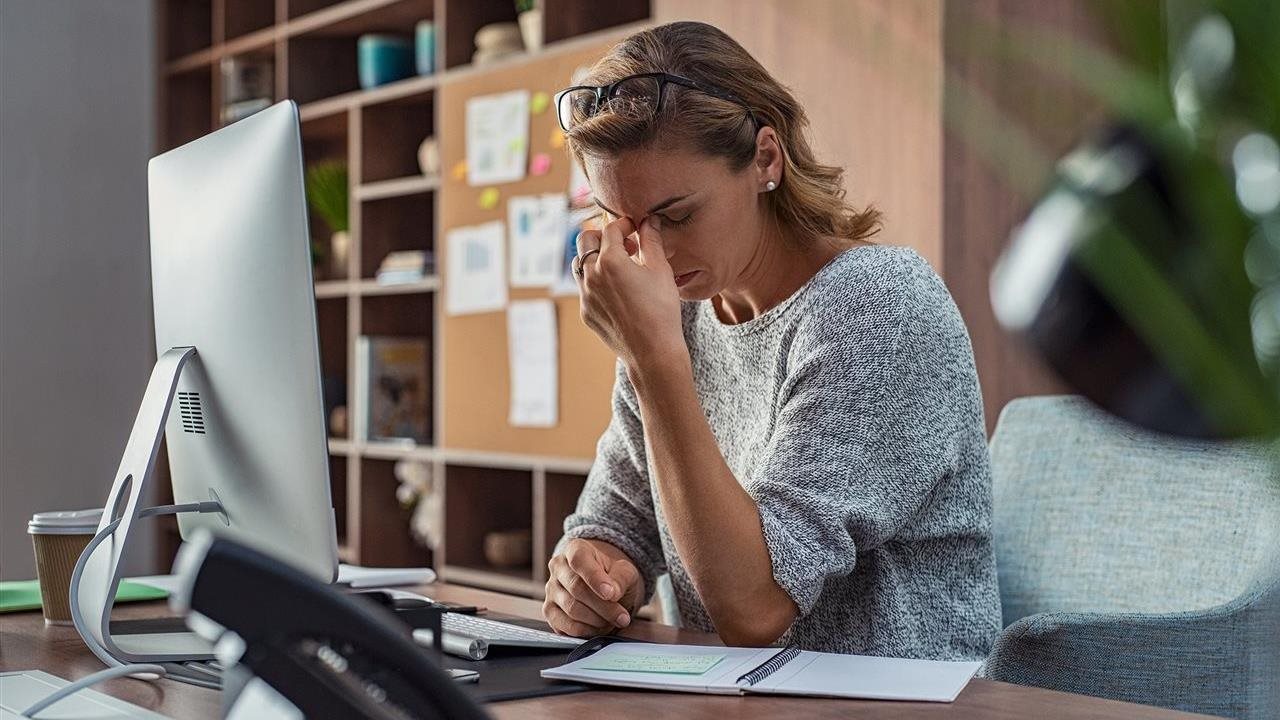 Woman working at her desk in an office pinching her eyes closed in an attempt to relieve her dry eyes.