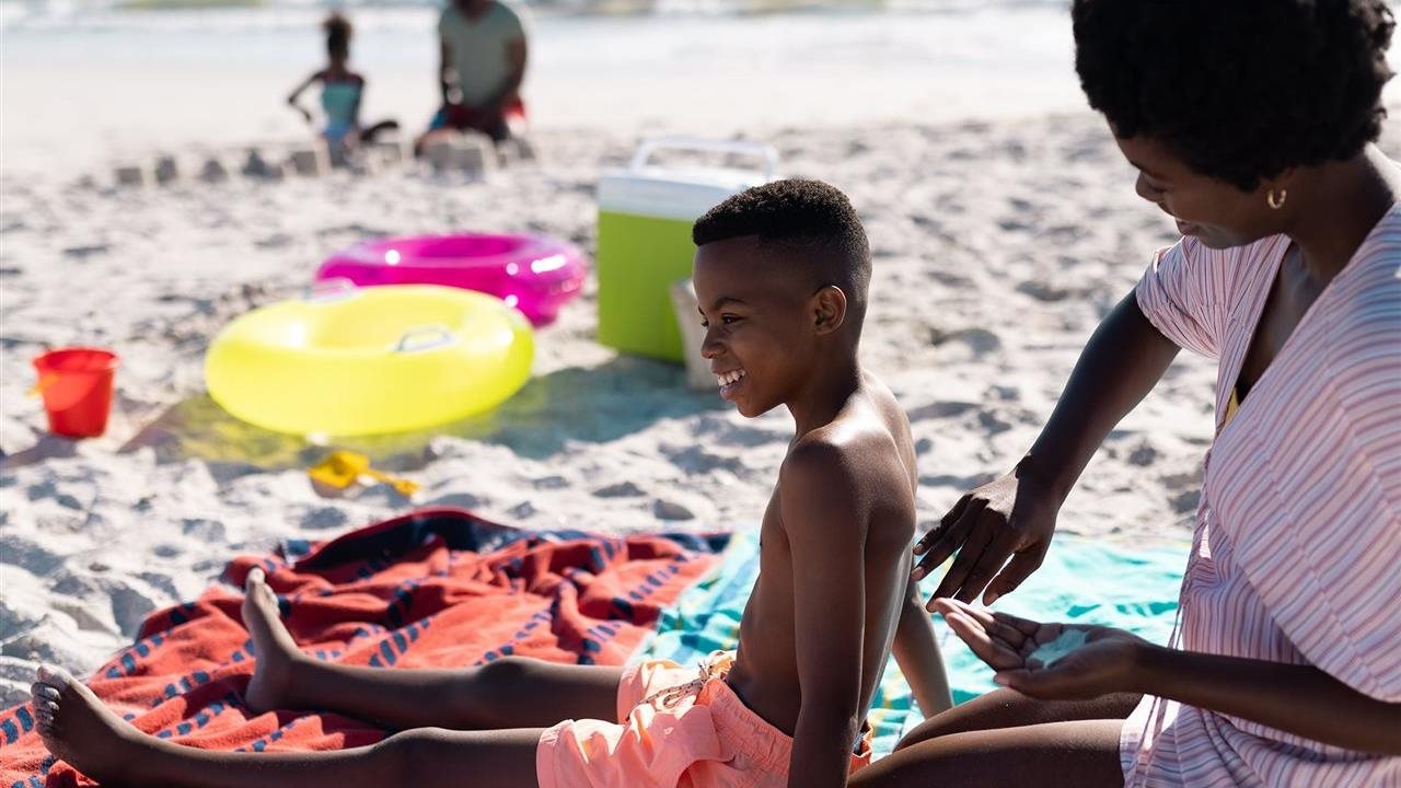 Mother applying sunscreen to son's back at the beach. Walgreens says use sunscreen to avoid sunburn.