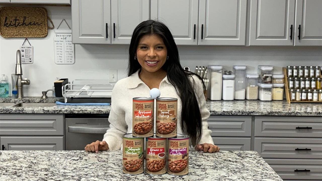 Jilliann Kupfer DeLawyer, senior director of marketing for Saucy Spoon Baked Beans. in the kitchen with stacked cans of Saucy Spoon Beans.