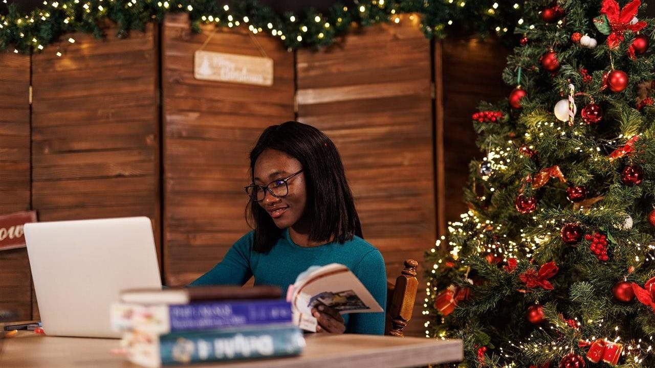 Young woman studying on-line using Sophia Learning subscribtion while sitting in a library next to a holiday tree.