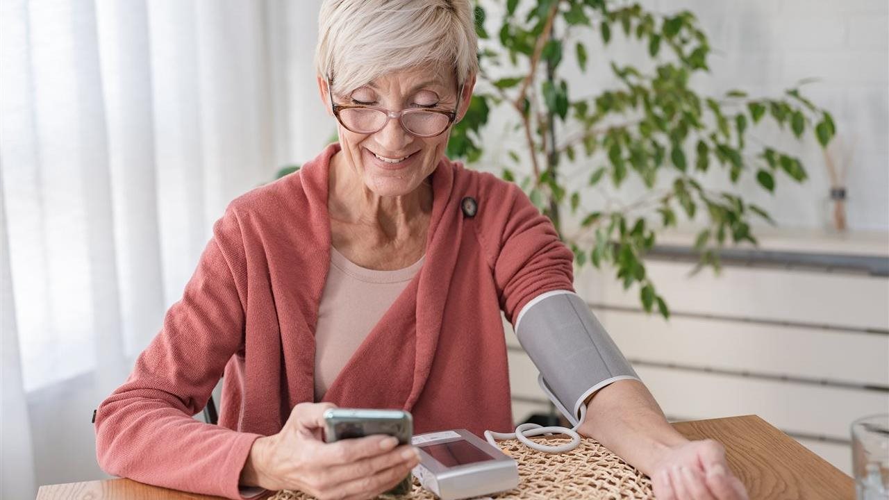 Senior woman takes blood pressure and uses phone app. Anthem Whole Health connects individual’s healthcare touchpoints.