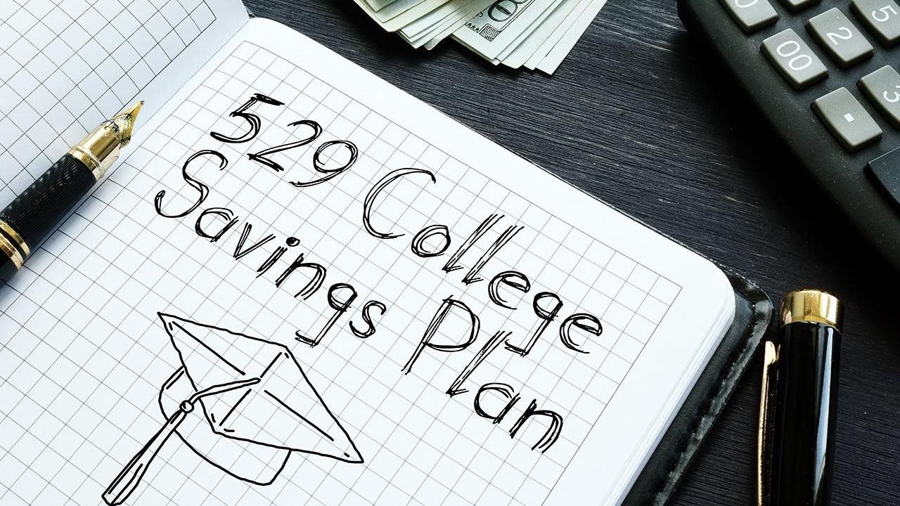 An open gridded journal with "529 College Savings Plan" written inside. Beneath it is a sketch of a graduation cap.