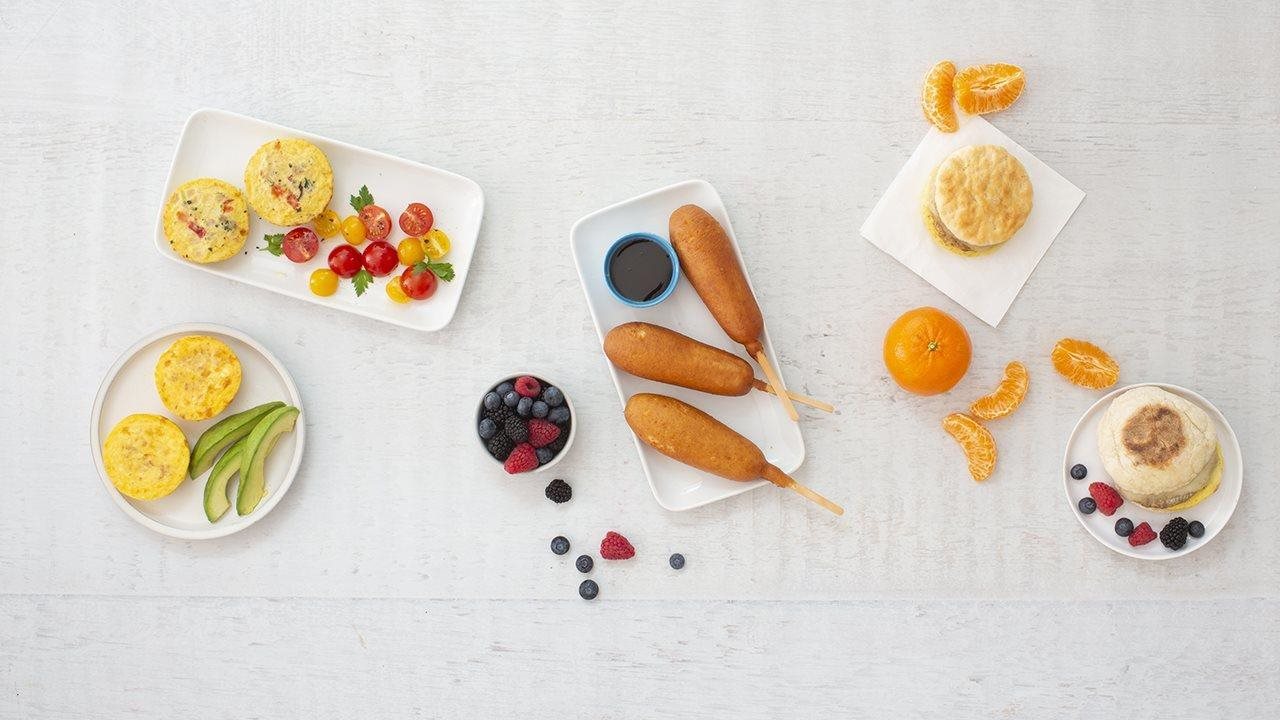 A collection of food including egg bites and corn dogs laid out on a white surface.